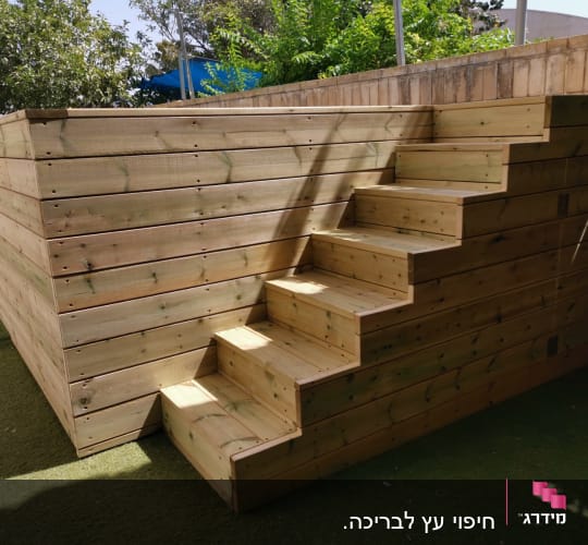 מדרגות עץ מובילות לגינה מוגבהת עם דשא סינתטי